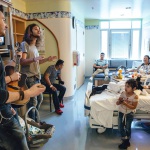 The band Levon plays for a family at a younger patient's bedside. The little sister of the patient shyly looks up at the band and smiles