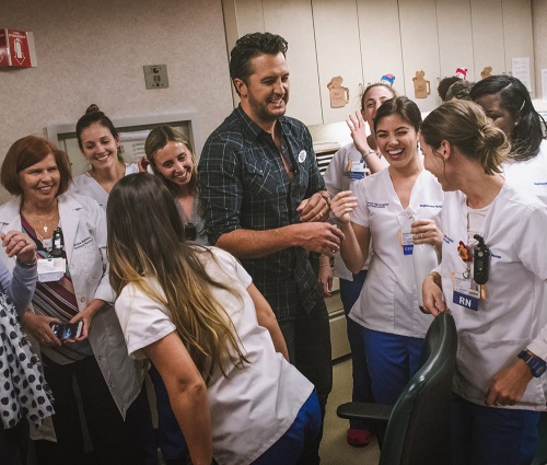 Luke Bryan laughs with caregivers and hospital workers at the launch of MOC Streaming, a program where donations of tablets, headphones and streaming subscriptions are sent to hospitals. Luke performed bedside at this event
