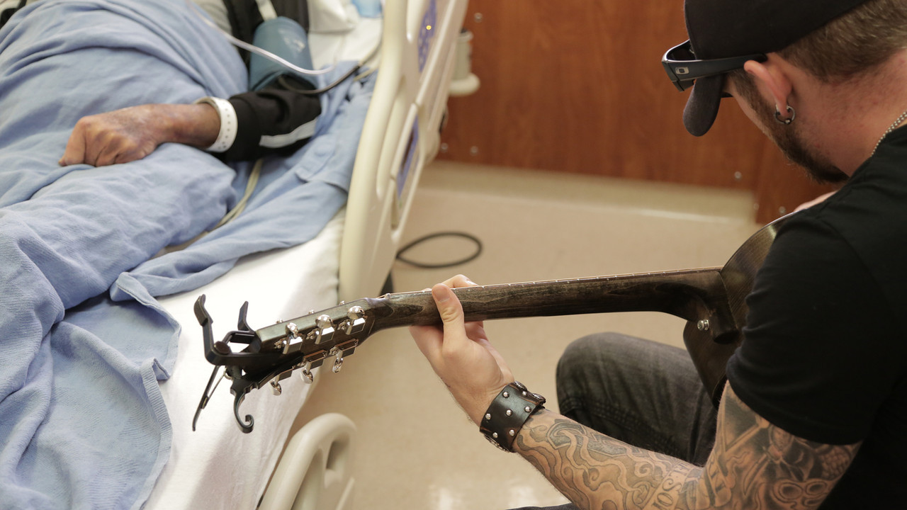 Musician plays bedside for a patient. Image is from the viewpoint behind the musician, no faces are visible.