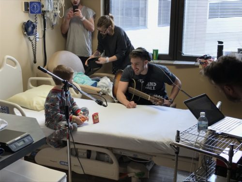 volunteers record their song with a patient. a microphone and shaker are set up for the patients to use. one volunteer is playing guitar and the other is managing the song recording