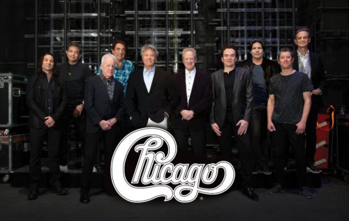 members of the band Chicago pose backstage at a concert. Their logo is displayed in front of them.