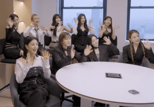 K-Pop idols TWICE wave at patients on a screen that is not viewable in the picture. They are all smiling and are excited to talk with superfan patients