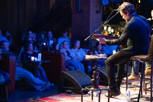 A backstage view of Charles Esten playing guitar as caregivers enjoy the concert