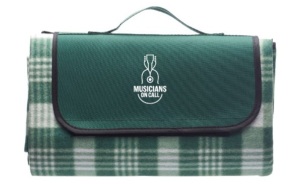 Image of the Musicians On Call picnic blanket you can receive when joining the Backstage Pass Club. It is a forest green plaid blanket that folds into its own carrying case with our logo on it, making it easy to bring with you to your picnic!