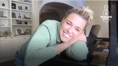 A screenshot of Rachel Platten smiling and leaning on her piano. She is listening to Scout tell his story of how 