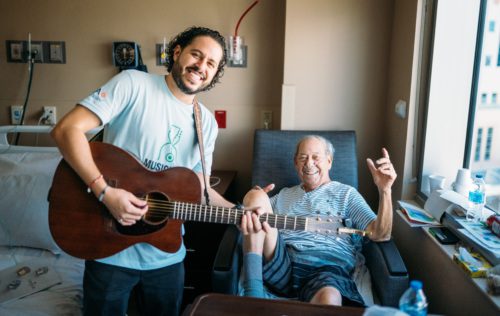Smiling musician volunteer poses next to happy patient.
