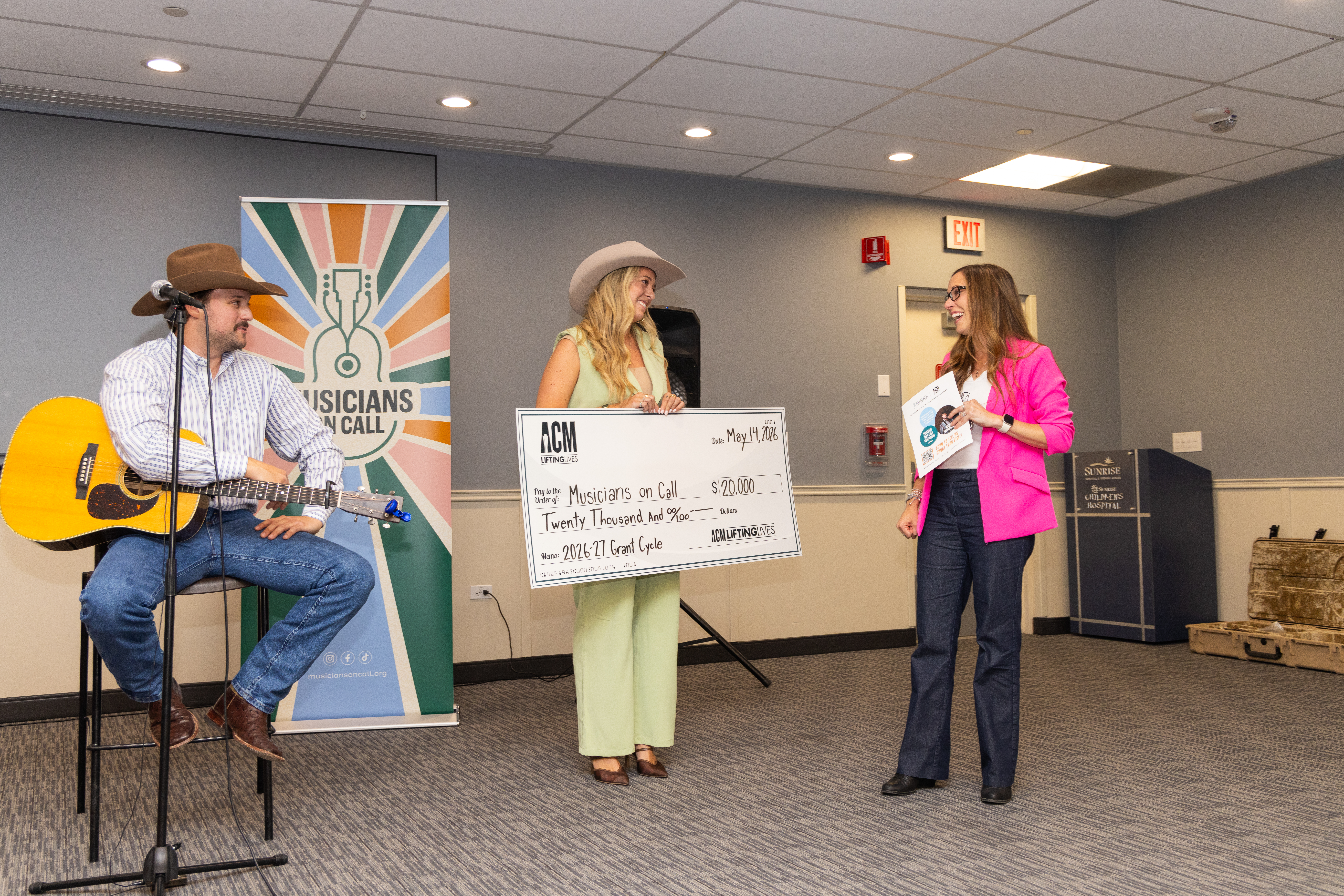 Walker Montgomery watches as Taylor Wolfe presents Katy Epley with a check for $20,000 for Musicians On Call.